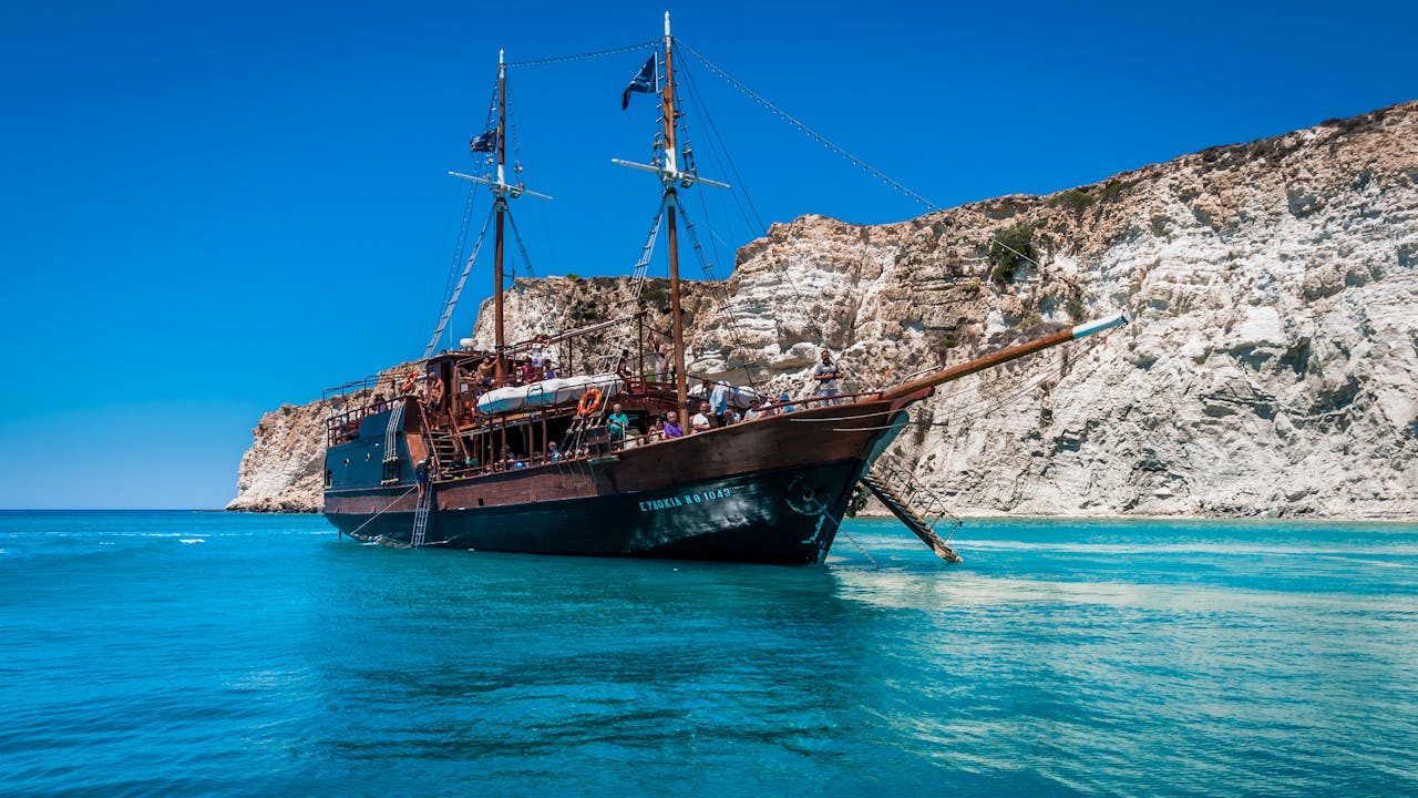 Pirate ship anchored near scenic cliffs in Lasithi, Greece with clear turquoise waters.